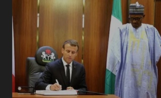 French President Emmanuel Macron (L) is watched by Nigeria’s President Muhammadu Buhari as he signs the ‘gold book’ at The Presidential State House in Abuja on July 3, 2018.